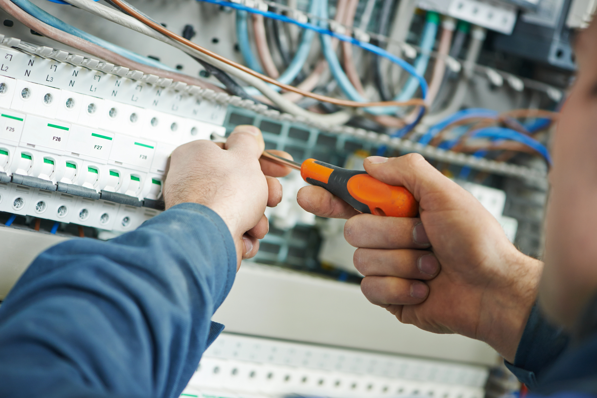 Close-up of an electrician using a screwdriver to work on wiring inside an electrical control panel.