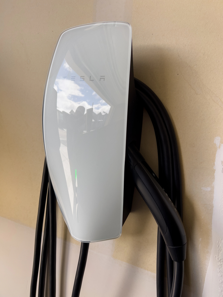 A white Tesla wall charger is mounted on a wall with its charging cable neatly wrapped around it.