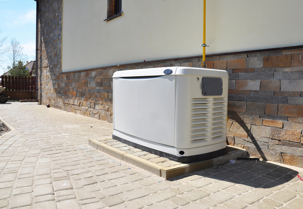 A standby generator is installed on a concrete pad next to a house with a brick and stone exterior wall.